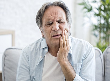 older man holding jaw in pain